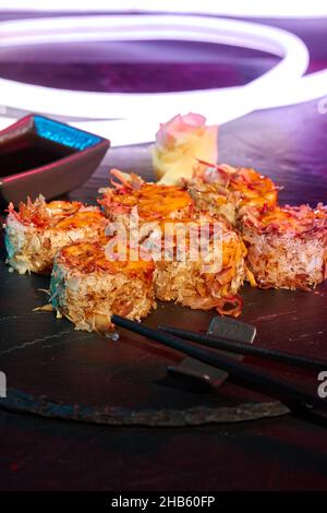 Closeup of uramaki rolls with melted cheese and bonito flakes on slate board with bright LED strip Stock Photo