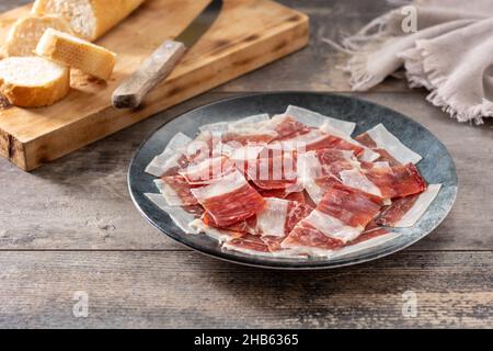 Spanish serrano ham slices on black plate on wooden table Stock Photo