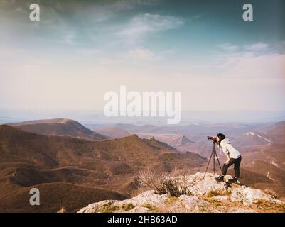 Side view young attractive caucasian hipster woman content creator photographing mountains with red girly DSLR camera on tripod Stock Photo