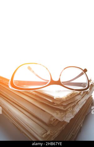 Stack old newspapers and reading glasses white background on a window on a bright sunny day Stock Photo