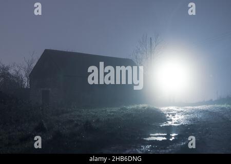 An abandoned barn back lighted on a foggy winters night in the countryside. Stock Photo