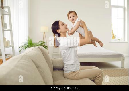 Portrait of happy cheerful young woman holding her baby and playing with her at home. Stock Photo