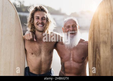 Happy fit surfers with different ages having fun surfing on tropical beach - Extreme sport lifestyle and friendship concept Stock Photo