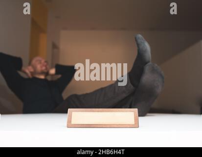 Person without shoes and and feets on the table sits relaxed at home in a living room with wooden business office plate and blank title space. Work fr Stock Photo