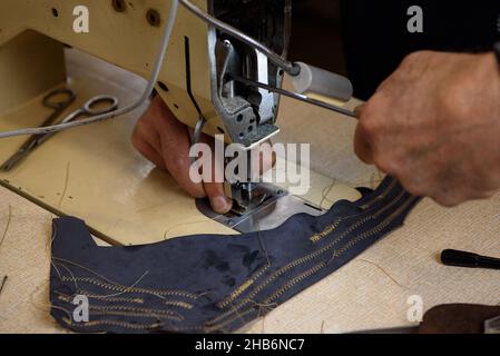 Mechanic repairing industrial sewing machine in factory. Hands of repairman fixing problems and testing professional overlock in shoemaker workshop Stock Photo