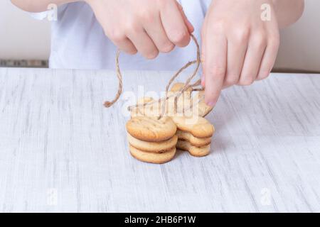 Children's hands are packing homemade Christmas gingerbread cookies on the table. DIY ideas for festive gifts. The child is packing a Christmas presen Stock Photo