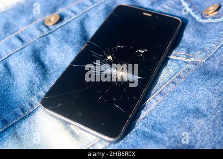 Broken mobile broken cell phone placed on dennim jacket Stock Photo