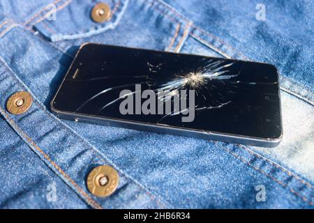 Broken mobile broken cell phone placed on dennim jacket Stock Photo