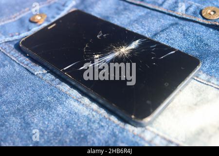 Broken mobile broken cell phone placed on dennim jacket Stock Photo