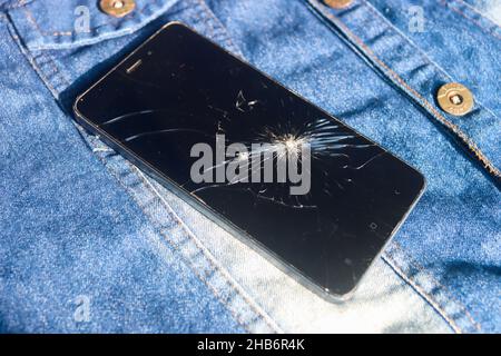 Broken mobile broken cell phone placed on dennim jacket Stock Photo