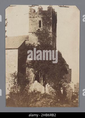 View of medieval church tower with battlements and part of church with cemetery, View of medieval church tower with battlements and part of church with cemetery. In the foreground a man in suit with top hat, looking into the camera., anonymous, c. 1875 - c. 1890, paper, albumen print, height 104 mm × width 76 mm