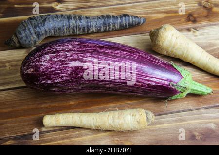 Top view on whole purple white ripe zucchini with parsley roots and black carrot on wooden background Stock Photo