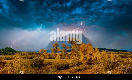 A surreal autumn landscape scene, as dramatic clouds and lightning fill the sky over the misty Teton mountain range in Jackson Hole, Wyoming, US. Stock Photo