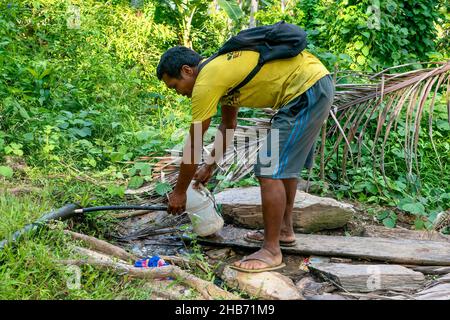 Puerto Galera, Philippines - Apr 24, 2021: An indigenous Mangyan man fills a plastic jug using a makeshift spigot cut into a municipal water pipe. Stock Photo