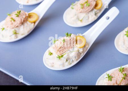 Cold appetizer made from cod liver, cod caviar, olives, cucumber and microgreens on serving spoons. Traditional cold dish. Close-up, blue plate, black Stock Photo