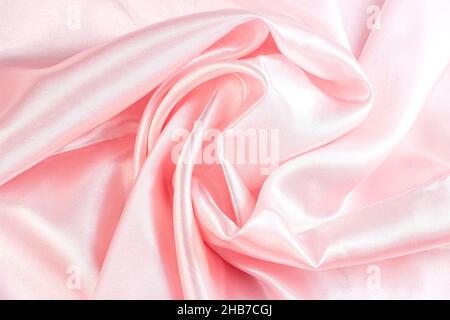 Light pastel pink color silk wavy textile pattern as a smooth textured background. Rose colored soft satin fabric drapery. Stock Photo