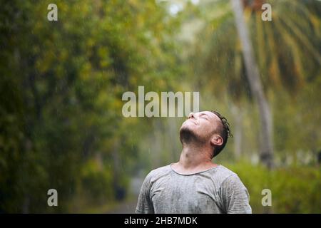 Portrait of drenched man with eyes closed enjoying heavy rain in nature. Stock Photo