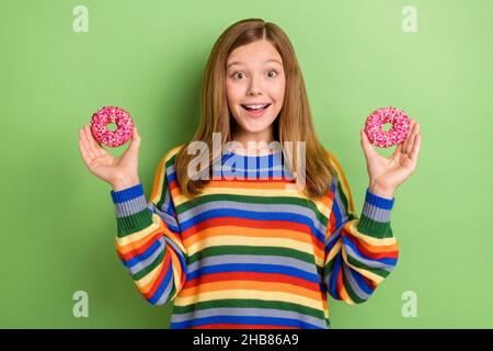 Portrait of attractive girly cheerful girl holding in hands two pink donuts isolated over bright green color background Stock Photo