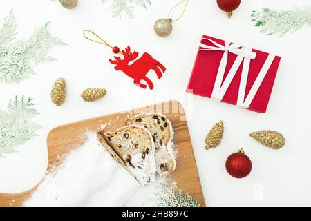 Christmas composition with stollen cake on a wooden board, tree toys and gift on white. Flat lay Stock Photo