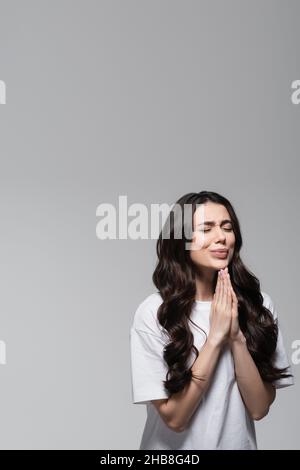 young woman with long wavy hair standing with praying hands isolated on grey Stock Photo