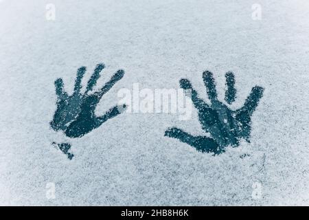 Imprint of two palm hands on the white snow texture. Two human handprints on frozen dark blue glass background. Concept of winter fun and cold weather Stock Photo