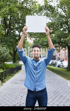 USA, New York, New York City, Portrait of man holding blank sign above head in city Stock Photo