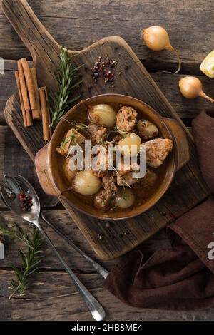 stifado - delicious mediterranean beef stew with onion bulbs, cinnamon and spices in a casserole, on a black wooden table, view from above, close-up Stock Photo