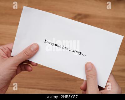 A woman holding a piece of paper with the words Everyone has a story written on it. Close up Stock Photo