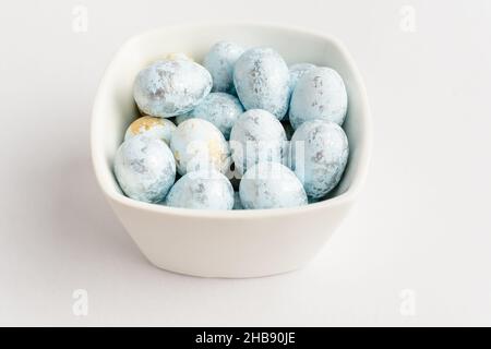 Blue chocolate coated Easter eggs candies on a bowl isolated on a white table, tasty sugary dessert for children Stock Photo