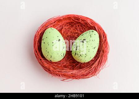 Two green colored decorative Easter eggs in a red rustic basket isolated on a white table Stock Photo