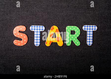 Card with Start word made from mixed vivid colored wooden letters on a textured dark black textile material that can be used as a message Stock Photo