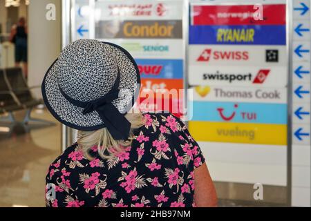 Palma, Spain - September 25, 2019: View from behind - unknown older woman with holiday hat at airport, blurred airlines logos in background, closeup d Stock Photo