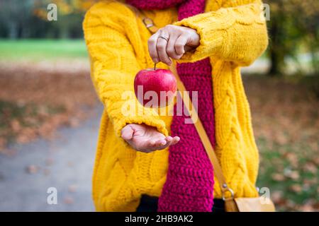 Woman holding red apple fruit in her hand. Fresh juicy apple as refreshment at autumn park. Stock Photo