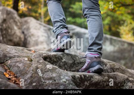 Woman is wearing hiking boot and walking on rocks in forest at autumn. Hiker climbing in mountain Stock Photo