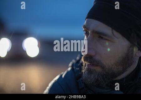 Man lost in thought, outside at dusk with car headlights in the background Stock Photo