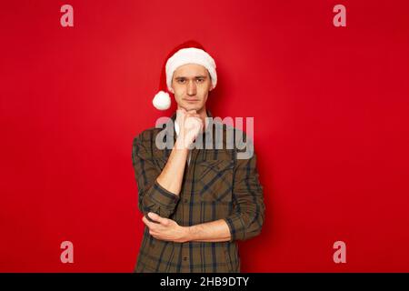 man holds chin his hand in thoughtful pose makes difficult choice isolated red background copy space Stock Photo