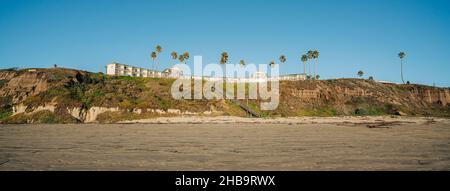 Cliffside beach, palm trees, and silhouette of hotel. Clear blue sky background, copy space Stock Photo