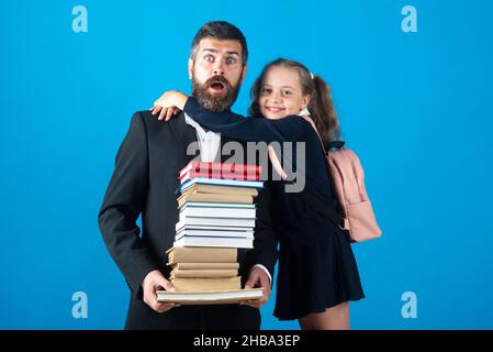 Elementary pupil hugging teacher in studio. Father or teacher with school girl daughter hold big stack school textbook notebook books. Teachers day. Stock Photo