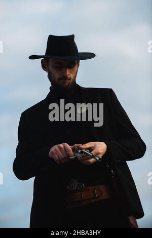 Cowboy shooter in black suit and cowboy hat. Serious man with wild west guns, retro pistol revolver and marshal ammunition. American western Sheriff Stock Photo