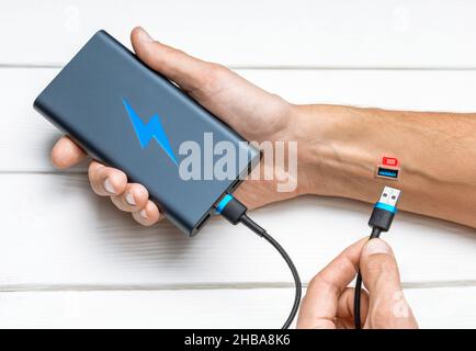 Man is charging from the power bank. The concept of a discharged battery or a decline in strength, the person is tired. Replenishment of energy reserves. Stock Photo