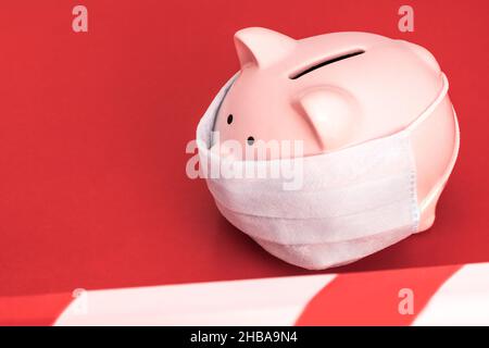 Pink Piggy Bank stands  on a  red background wearing medical face mask, the red and white ban tape is stretched. Chinese Coronavirus , 2019-nCoV Stock Photo