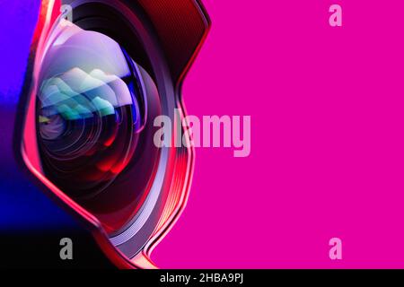 The camera lens with bright pink and blue  backlight. Close-up of the camera lens on a red  background. Optics. Stock Photo