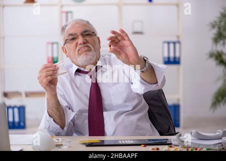 Old male drug addicted employee sitting at workplace Stock Photo