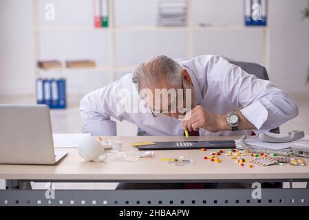 Old male drug addicted employee sitting at workplace Stock Photo