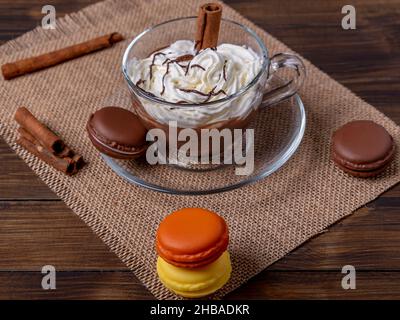 A glass cup with hot chocolate and cream on top on a table with some colorful macarons Stock Photo