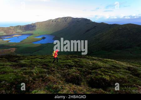 Woman with yellow backpack walking at Caldeirao crater at sunrise, Corvo island, Azores, Portugal Stock Photo