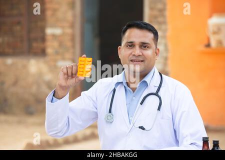 Portrait Of Young Indian Male Doctor Wearing Stethoscope Holding Medicine. Rural Healthcare Concept. Stock Photo