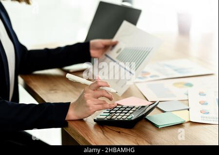 A businesswoman using a calculator and holding a graph, a woman holding a graph in her hand using a calculator, a young woman analyzing data graphs wi Stock Photo
