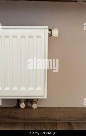 A part of a radiator of a central heating system. The radiator is white and with a grill and at the top right a know to regulate the warmth being disp Stock Photo