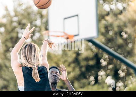 Selective focus on a woman shooting a ball at the basket while a man defends it Stock Photo
